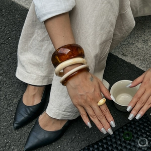 Dettaglio di bracciali e anelli in resina marmorizzata color ambra e bianco latte
