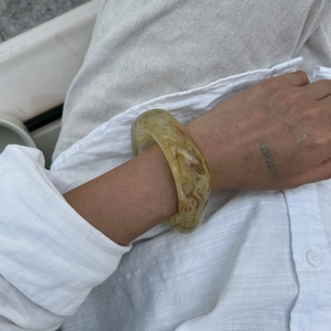 Detail of wide translucent resin bangle with amber marble texture worn by a model