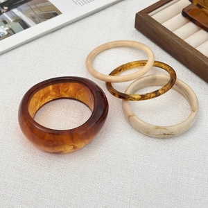 Dettaglio dei bracciali in resina con trama ambra e motivi marmorei minimalisti