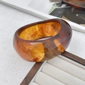 Dettaglio di un ampio bracciale in resina ambrata tartarugata con venature naturali su vassoio