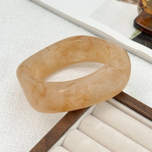 Macro shot of thick amber acrylic bangle with marble pattern on a velvet jewelry stand