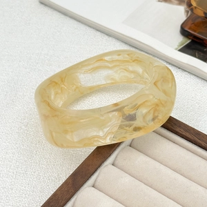 Macro view of wide acrylic bangle featuring amber marble texture on a wood display