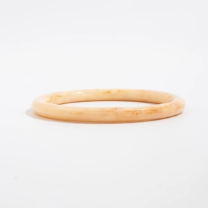 Dettaglio di un ampio bracciale in resina con trama marmorizzata arancione chiaro e finitura