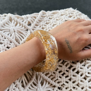 Macro detail of wide resin bangle featuring irregular gold foil flakes and smooth finish