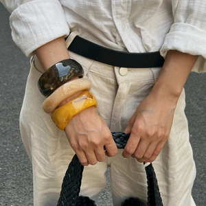 Primo piano di braccialetti in resina ambrata e borsa in pelle intrecciata nera all'aperto