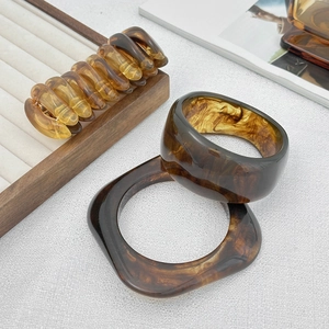 Détail de bracelets en résine ambrée et pince à cheveux posés sur un plateau à bijoux