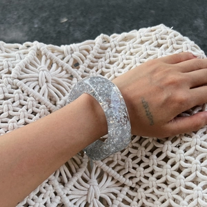 Detail view of transparent resin bangle with silver foil flakes on hand with white textile