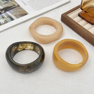 Dettaglio di ampi bracciali in resina nei colori ambra, crema e tartarugato