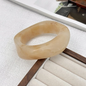 Dettaglio di un ampio bracciale in resina marmorizzata con motivi a spirale crema
