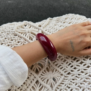 Close-up of a wide polished dark red resin bangle on a white woven fabric background