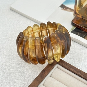 Gros plan d'un bracelet extensible en acrylique ambre translucide sur surface blanche