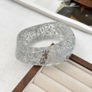 Close-up of wide transparent resin bangle with embedded irregular silver flakes on a tray