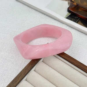 Macro detail of a wide pink resin bangle with white marble texture on a wood display tray
