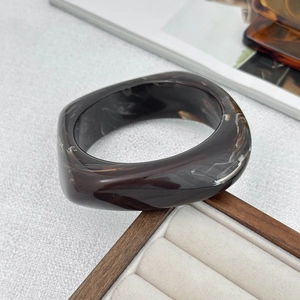 Macro shot of dark brown marbled resin bracelet with thick geometric design on velvet tray