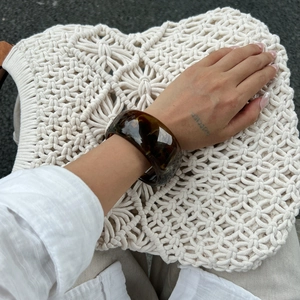 Detailed view of wide tortoiseshell acrylic bangle on model with woven bag backdrop