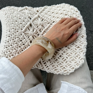 Detail of wide resin bracelet featuring marble texture worn with a white knit bag