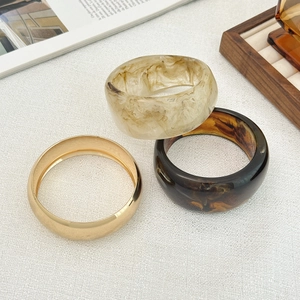 Close-up of stacked acrylic resin and gold metal bracelets with marble and tortoise patterns