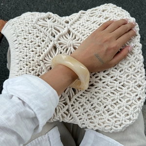 Irregular chunky amber resin bangle with marble texture displayed on a woven bag