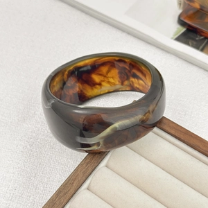Detail of amber tortoiseshell wide resin bangle resting on a minimal jewelry box