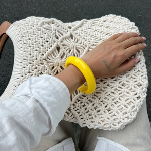 Detail van een heldergele brede hars armband gedragen op een witte geweven tas