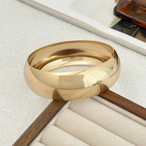 Close-up of a wide polished gold metal cuff bracelet resting on a velvet jewelry box