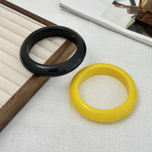 Detailopname van dikke gele en zwarte hars armbanden op een houten sieradendisplay