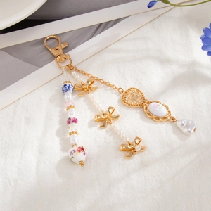 Elegant floral porcelain keychain with gold bow and pearls on a white linen background