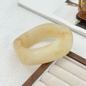 Macro detail of wide resin bangle with creamy marble pattern on a luxury white display