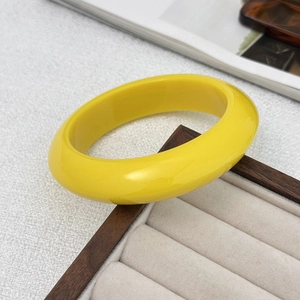 Detailopname van glanzende felgele brede hars armband op een houten sieradenhouder