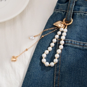 Detail of white pearl bead strap with gold heart pendants on blue denim jeans