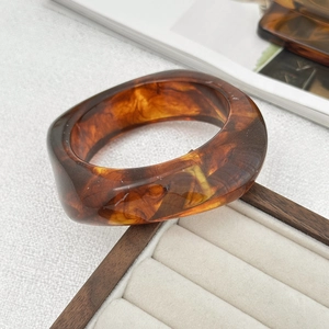 Detail view of a chunky amber resin bangle with marbled pattern on a wooden display
