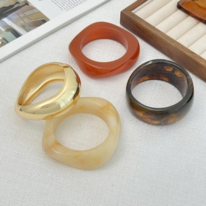 Detail of chunky acrylic and gold metal bangle set featuring amber and marble textures