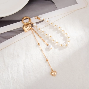 Ceramic pearl keychain with gold heart charms and tassel on white textured fabric