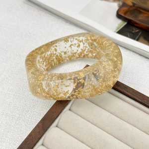 Macro detail of translucent resin bangle with embedded gold foil flakes on velvet display