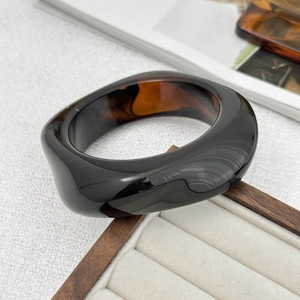 Macro shot of wide acrylic resin bangle showing polished black finish and amber texture