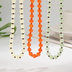 Detailweergave van de lichtgroene, oranje en crème glaskraalkettingen met bruine tussenkralen