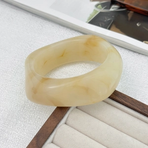 Detail view of a wide cream acrylic bangle with marble texture on a wooden tray