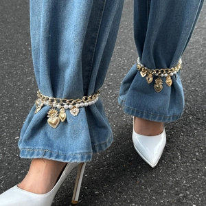 Detail of layered gold metal chains with pearls and retro pendants on blue jeans