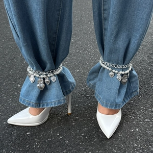 Detail of double-layer ankle chain with silver hearts and pearls on denim jeans
