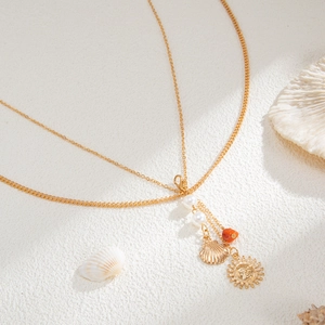 Detail of layered gold body chain with shell pendants and pearls on a beach sand background