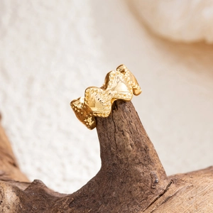 Makroaufnahme goldener C-förmiger Ohrring mit Muscheltextur und künstlerischem Wellendesign