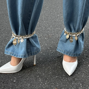 Detailed view of gold chain anklets with heart charms and pearls on denim jeans