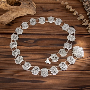 Macro detail of vintage silver waist chain featuring hollow floral carving and heart pendant
