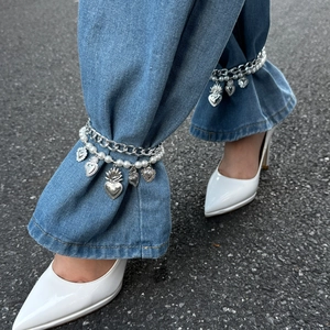 Detail of silver chain anklet with faux pearls and heart charms on denim jeans
