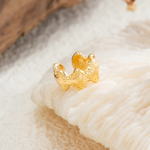 Macro detail van gouden ear cuff met organisch bloemen- en oceaanrimpelontwerp