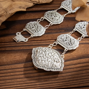 Detail of vintage silver waist chain with floral relief on textured wood background