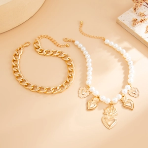 Detail of gold chain bracelet and faux pearl heart pendant necklace set on pink background