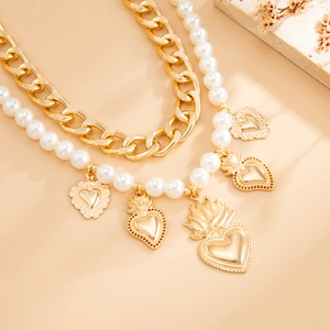 Detail of layered gold cuban link chain and faux pearl necklace with heart charms