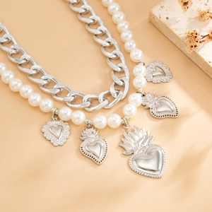 Detail view of silver metal chain with heart charms and faux pearls on a stone block