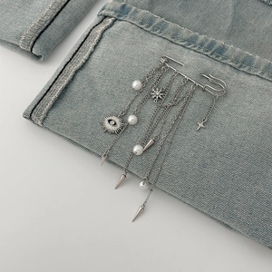 Punk style silver safety pin brooch with devil eye pendant, pearls and spikes on denim